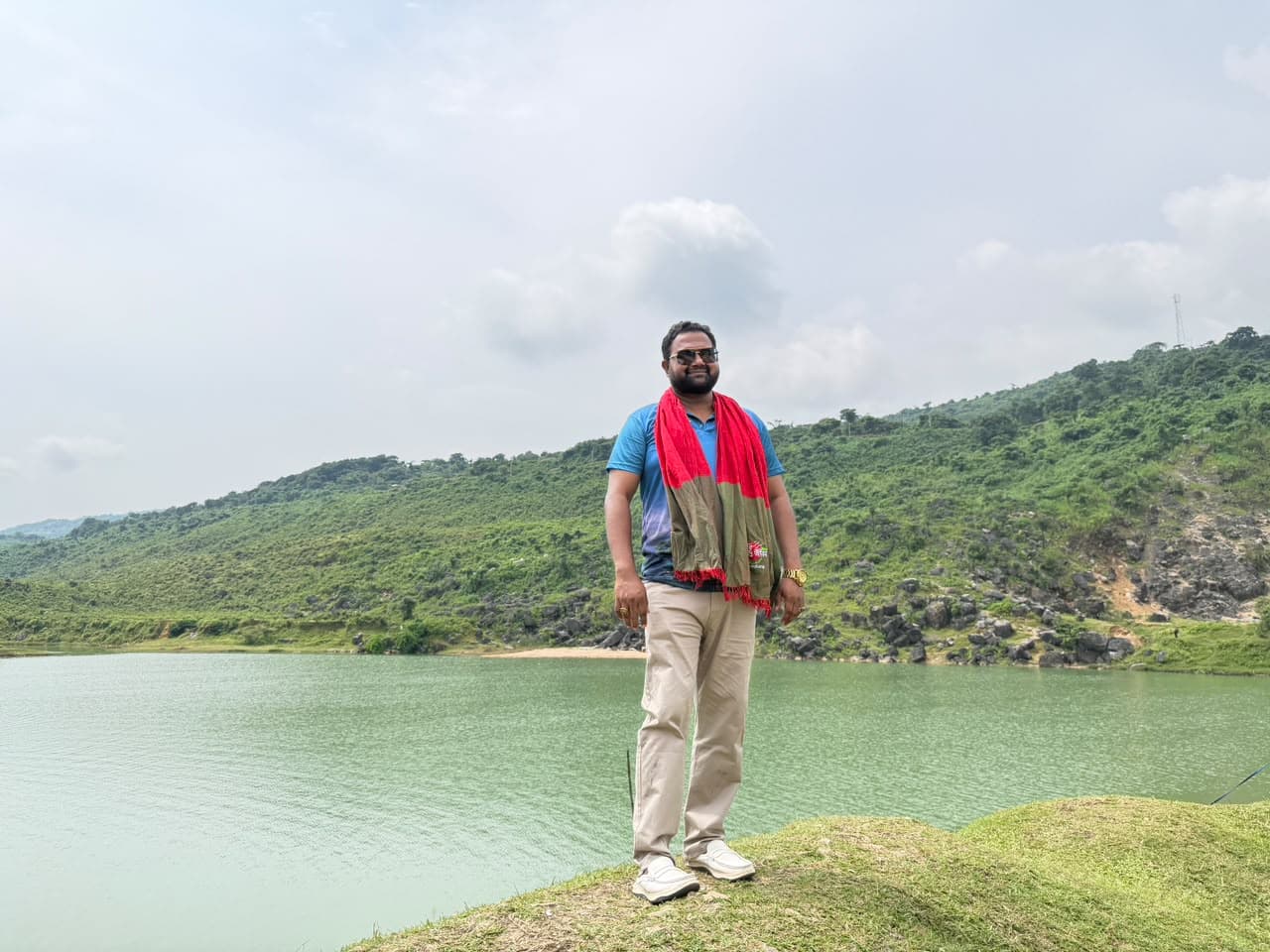 Md. Abu Jubayer standing beside green water with wooded hills in the background
