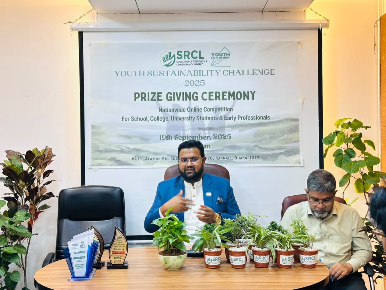 Md. Abu Jubayer speaking at the Youth Sustainability Challenge prize-giving ceremony, with plants and awards on the table